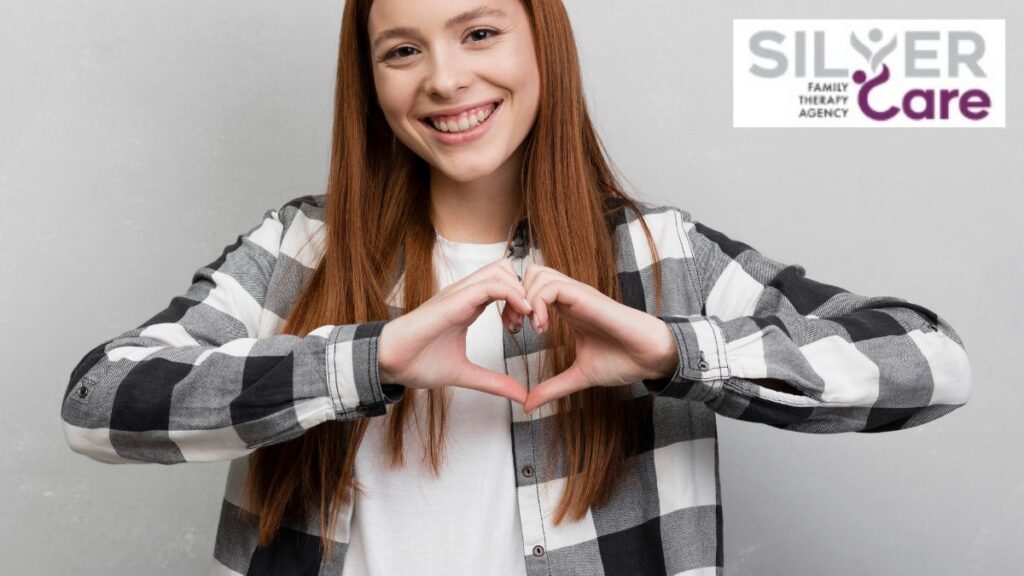 Teen girl smiling at the camera while forming a heart shape with her hands, symbolizing self-esteem and self-love.