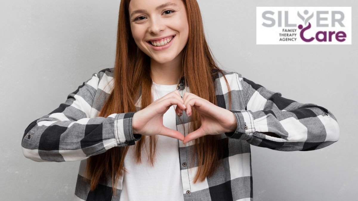 Teen girl smiling at the camera while forming a heart shape with her hands, symbolizing self-esteem and self-love.