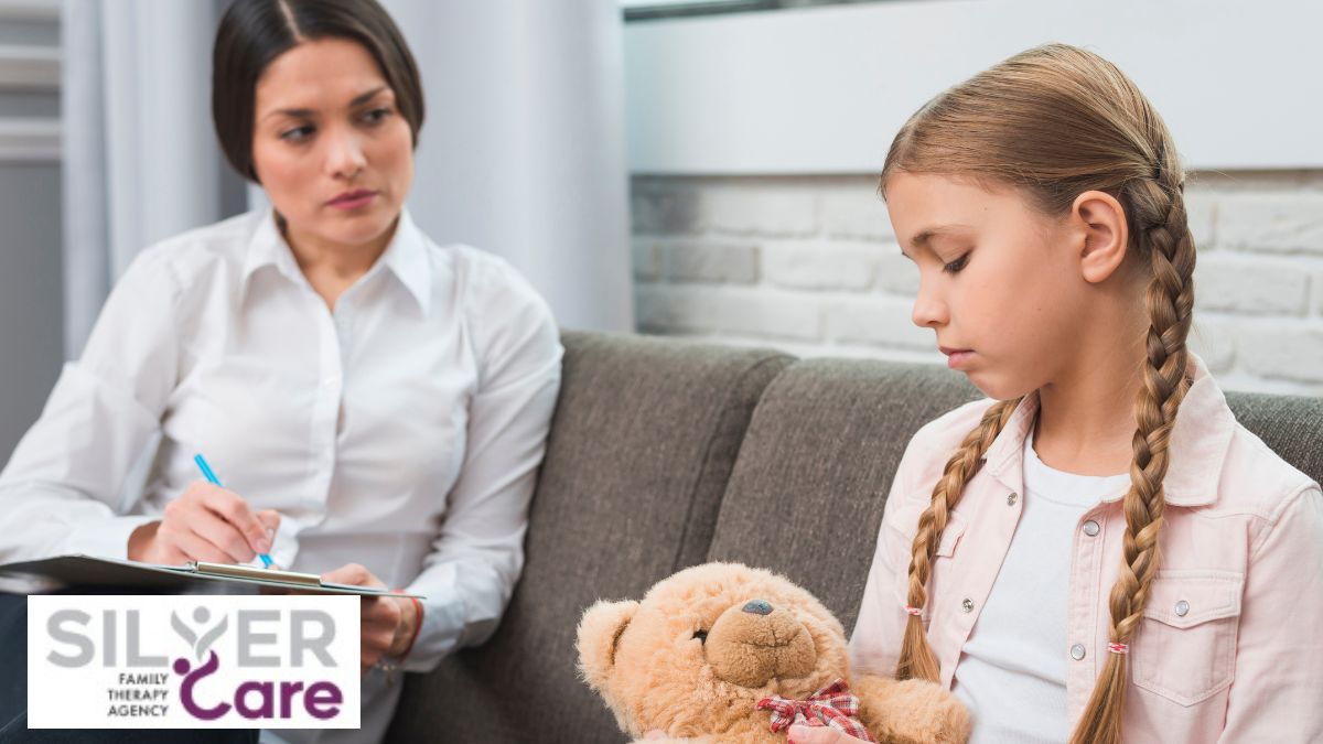 A therapist guides a child holding a plush bear, gently helping her express feelings.