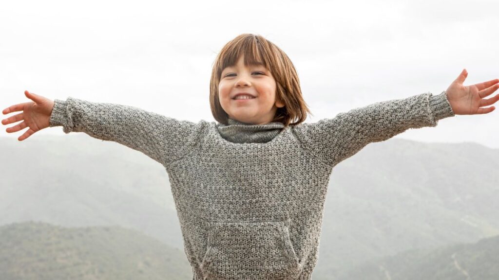 A young boy stands outdoors with arms wide open, experiencing exhilarating joy.
