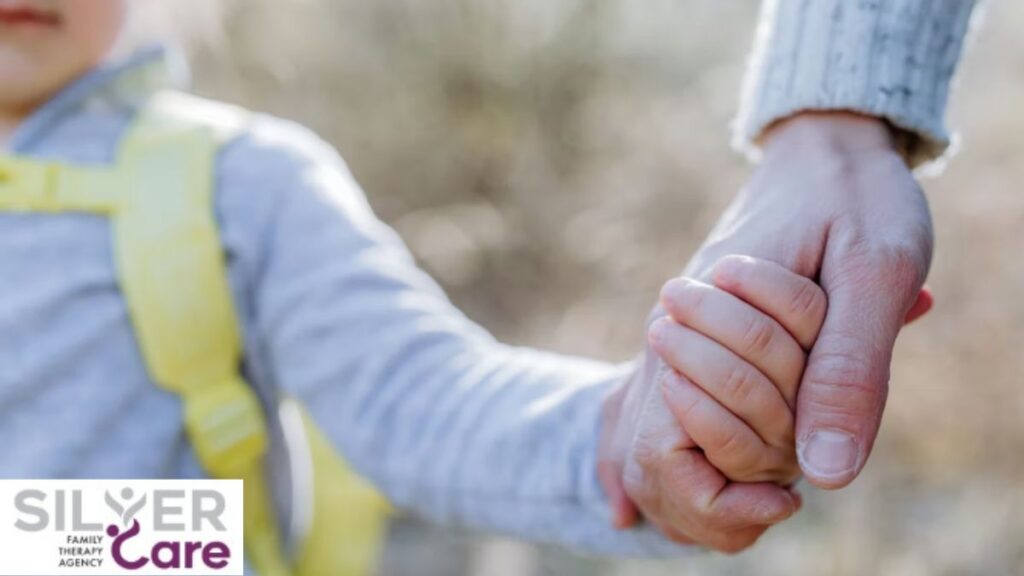 An adult’s hand gently guides a young child’s hand, shown in soft focus.