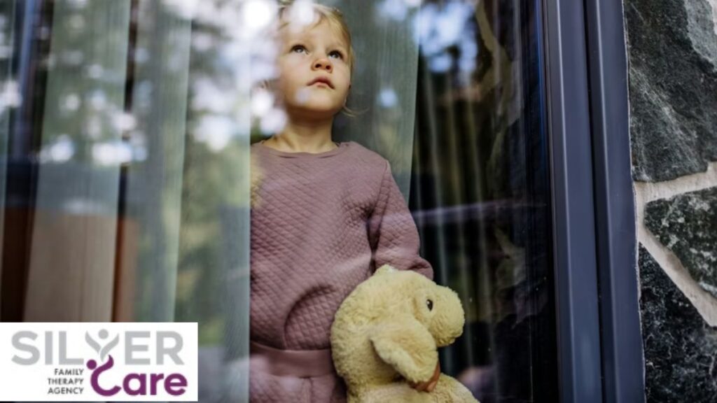 A young boy holding a plush bear gazes out a glass window, reflecting teen depression symptoms.
